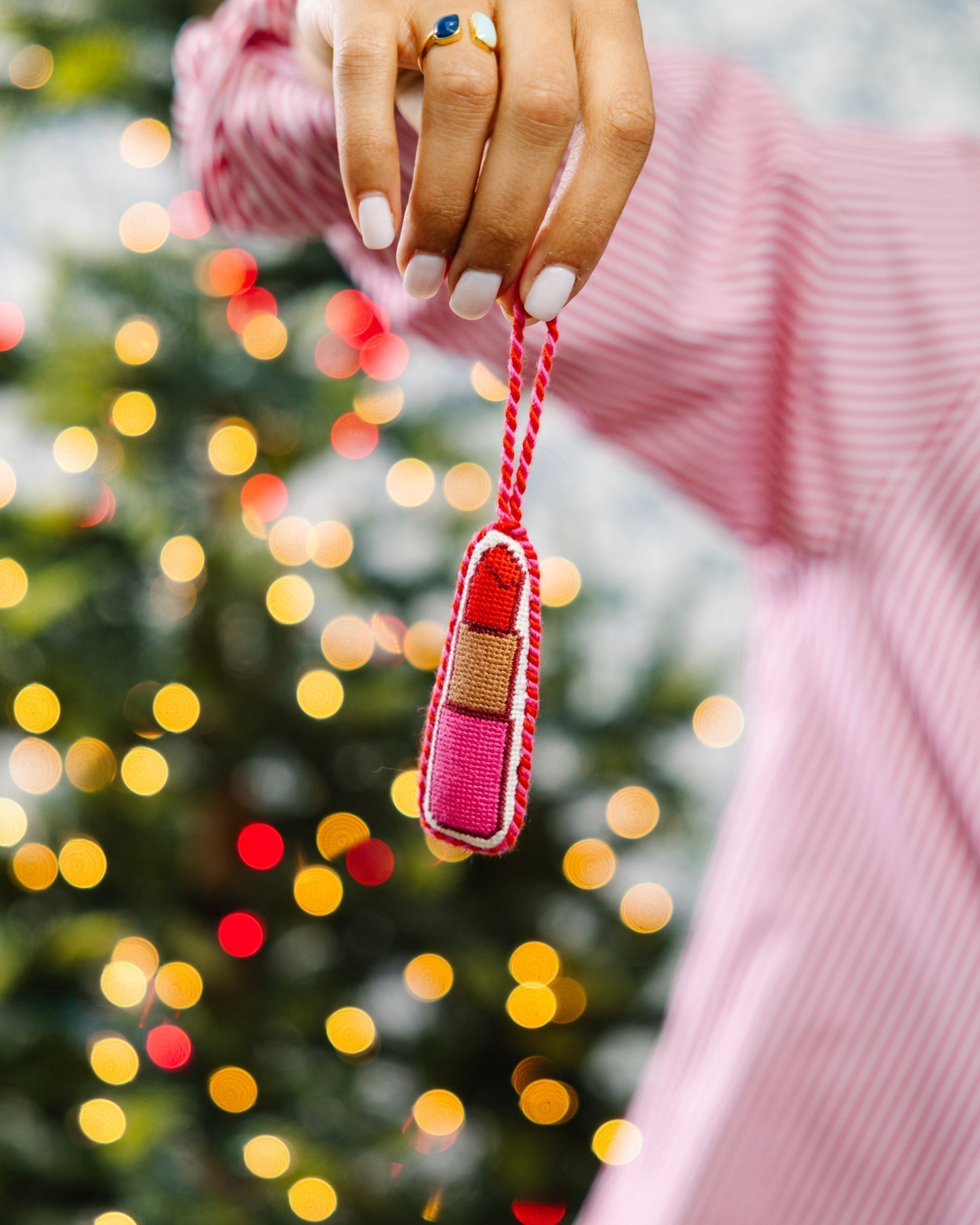 Hand holding a small red and pink keychain with a blurred Christmas tree in the background