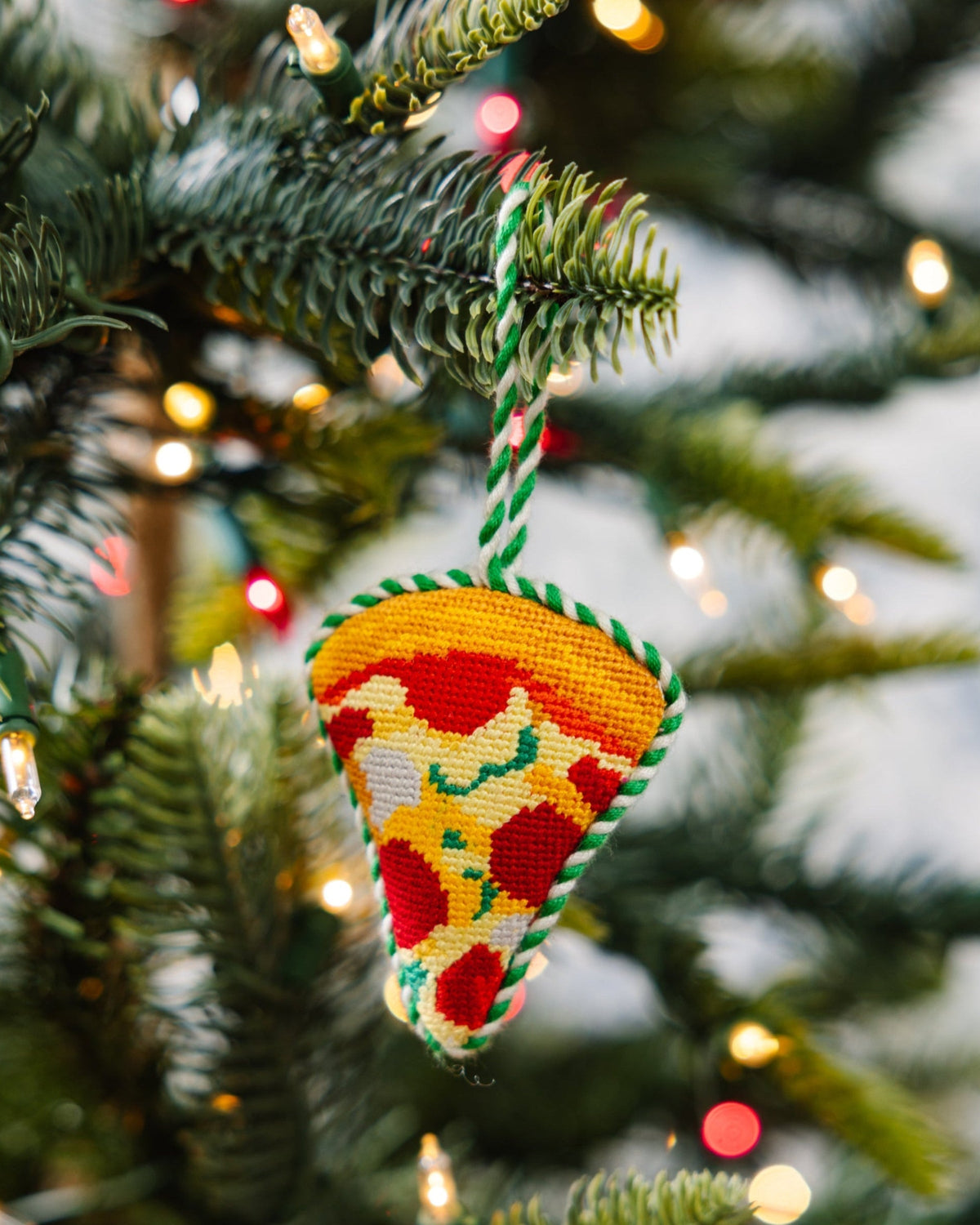Decorative pizza ornament hanging on a Christmas tree with lights in the background