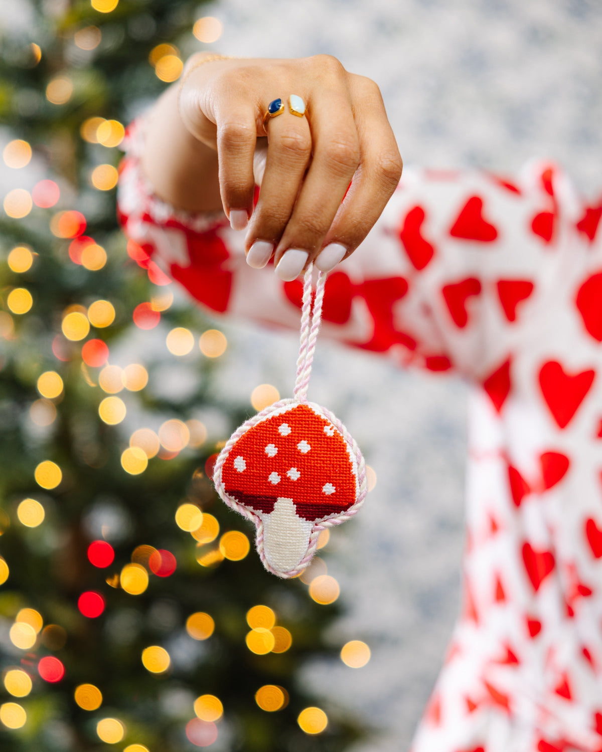 Hand holding a red and white mushroom ornament with a blurred Christmas tree in the background