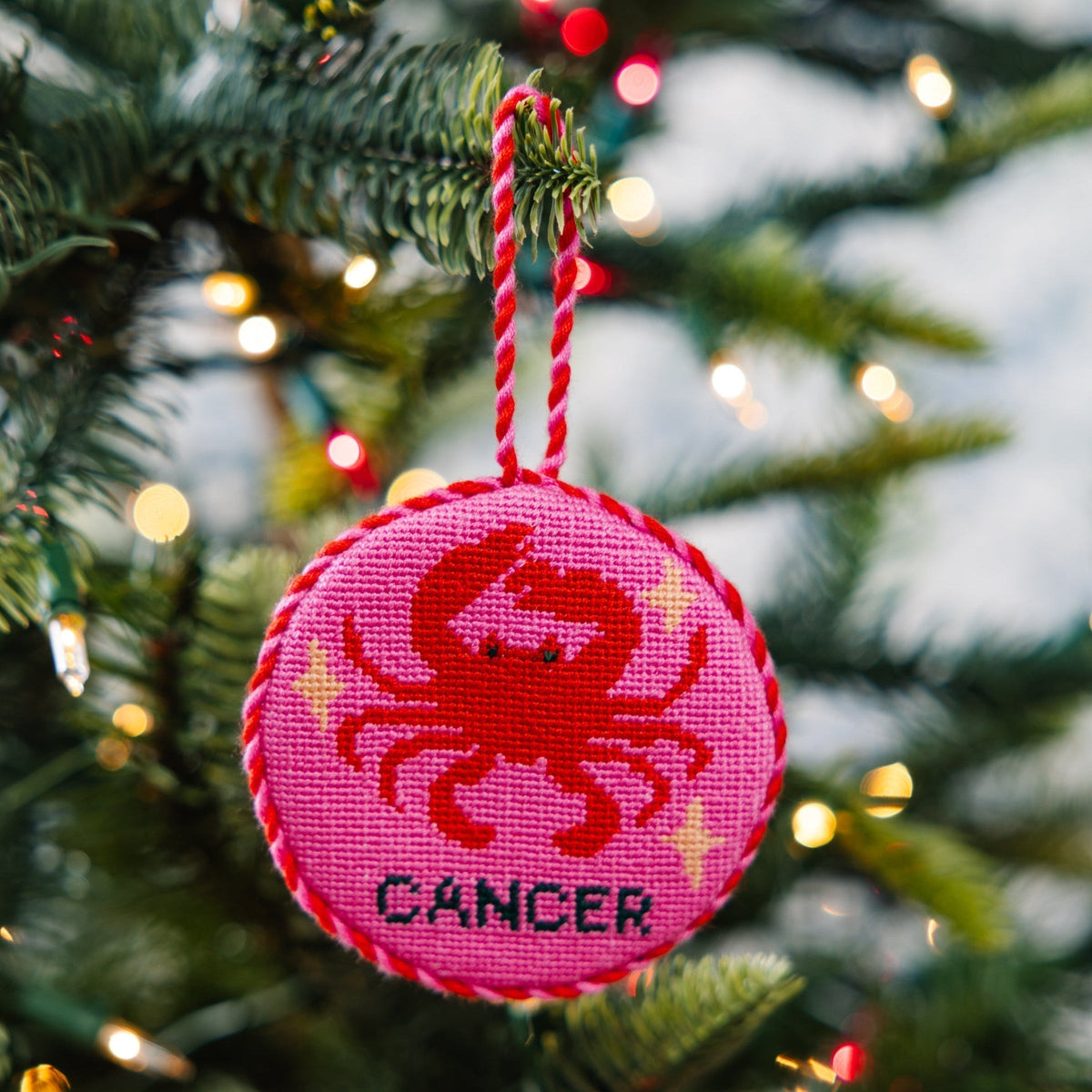 Decorative ornament with a red crab design and 'Cancer' text on a pink background, hanging on a Christmas tree.