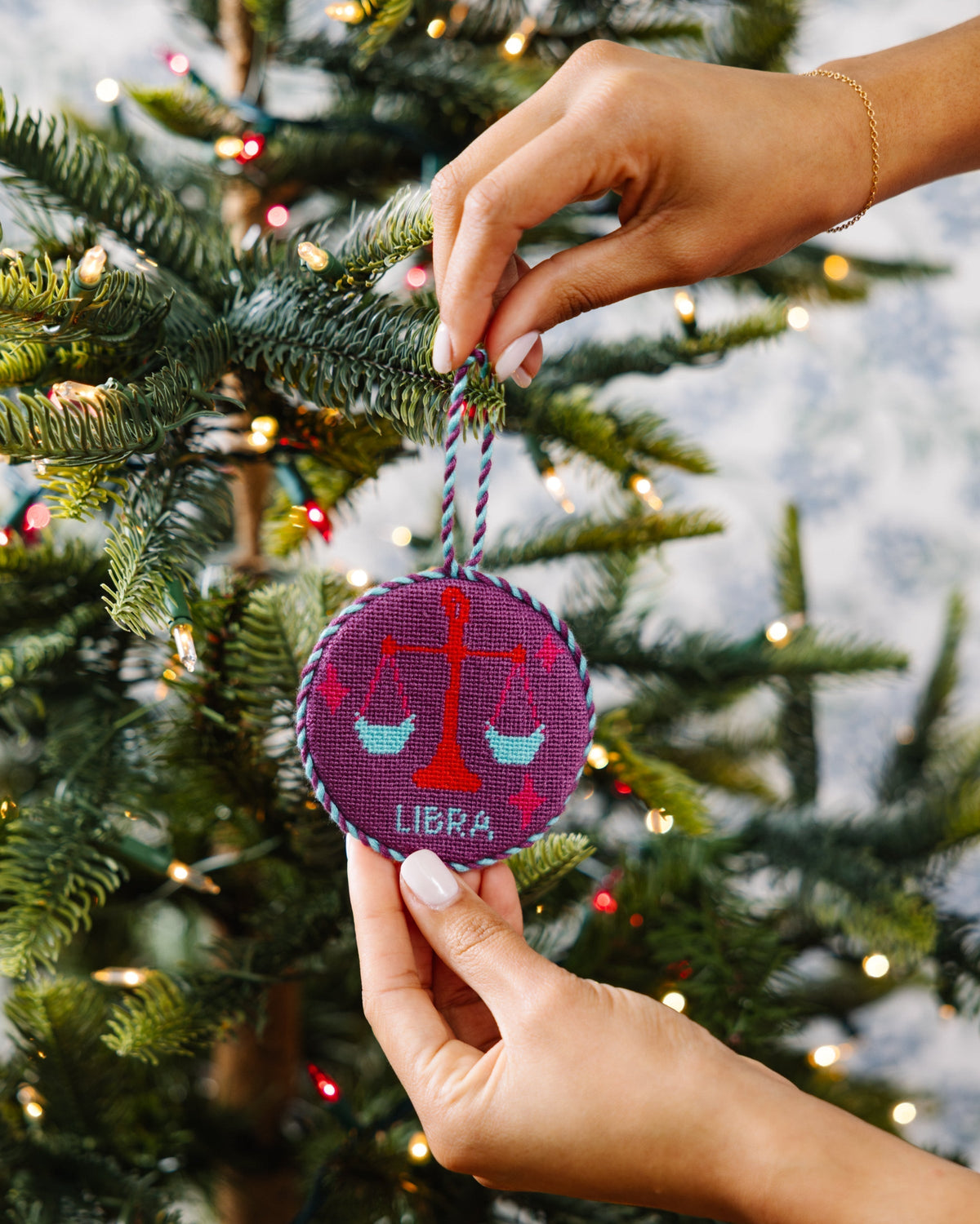 Hand holding a Libra zodiac ornament on a Christmas tree.