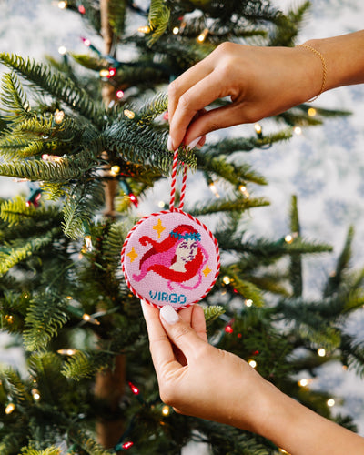 Hand placing a 'Virgo' themed Christmas ornament on a decorated tree.