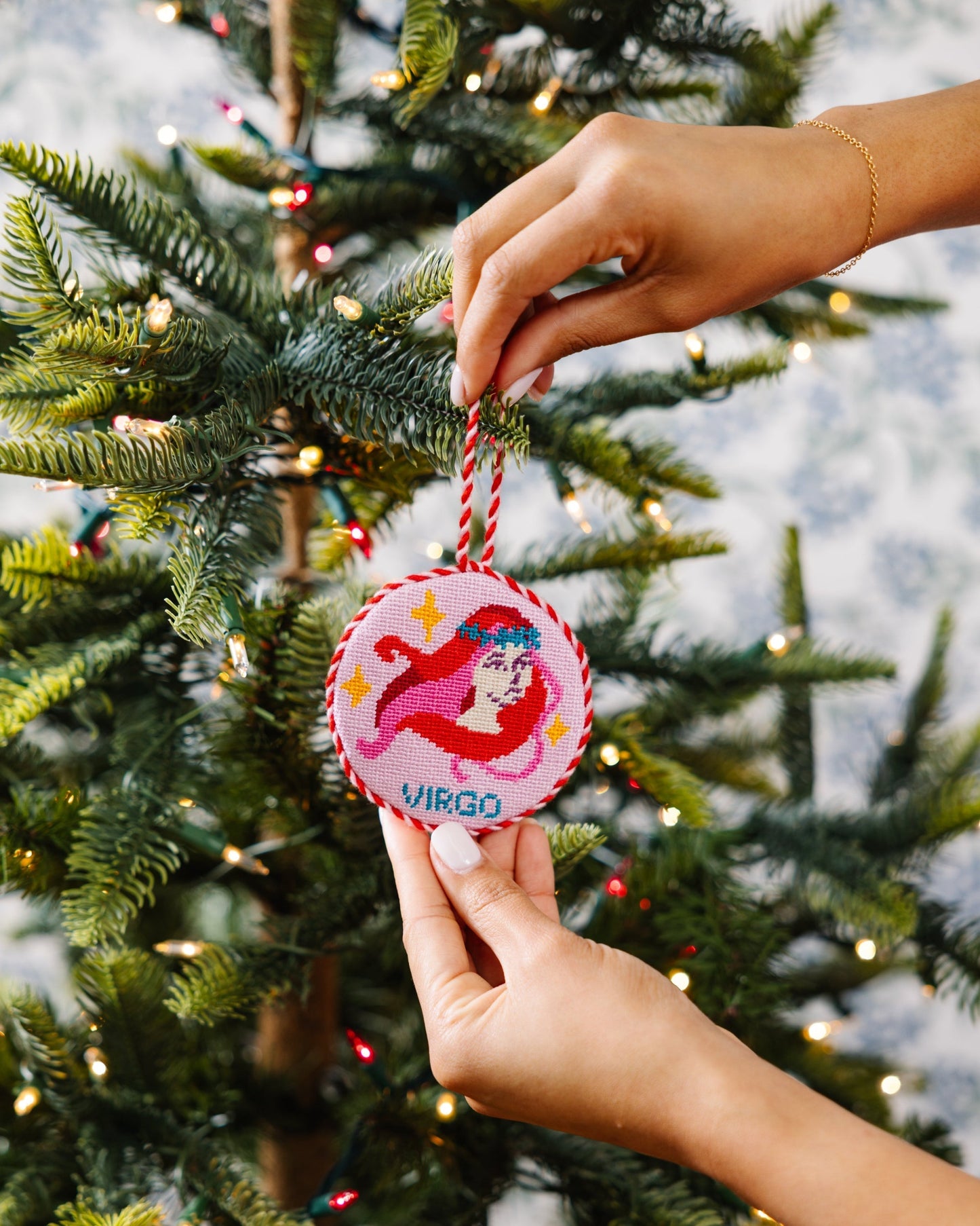 Hand placing a 'Virgo' themed Christmas ornament on a decorated tree.