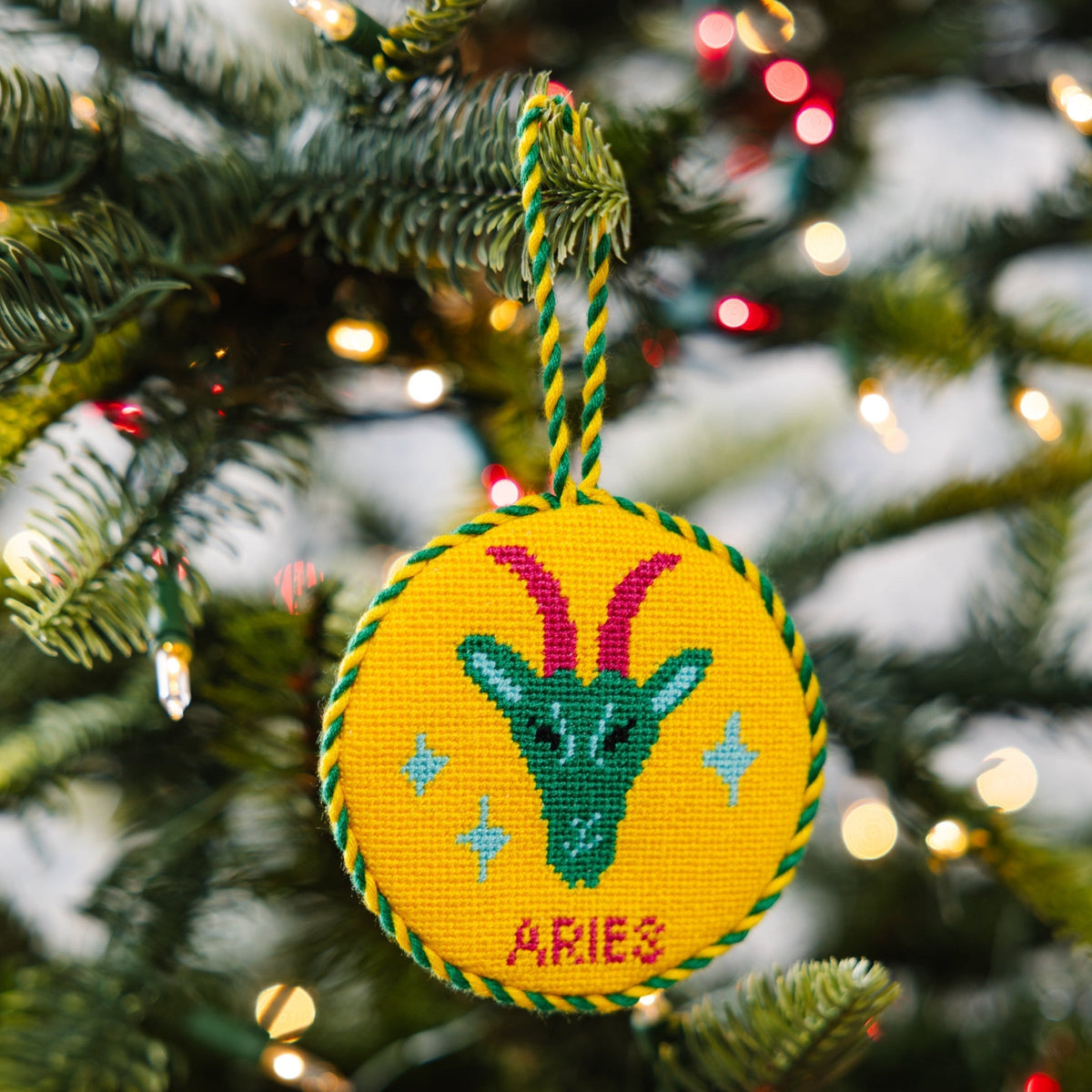 Decorative Aries zodiac sign ornament on a Christmas tree with lights in the background