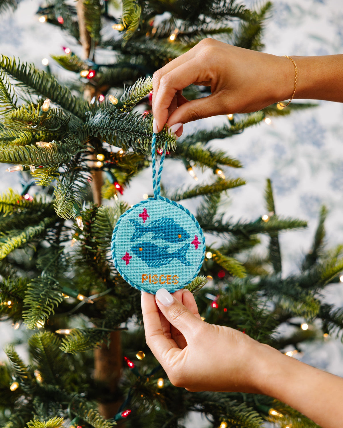 Hand holding a blue ornament with a whale design against a Christmas tree background