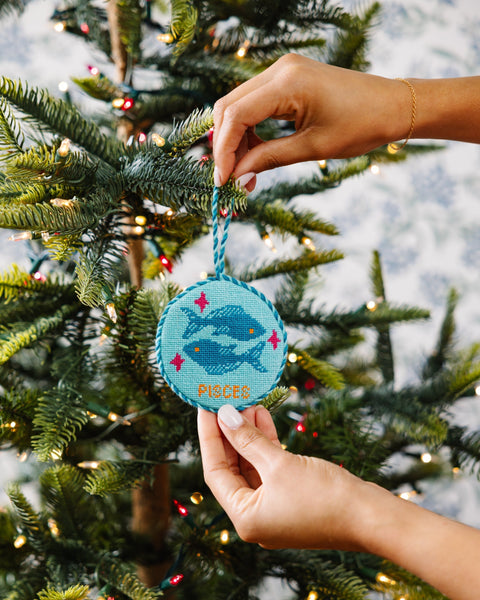 Hand holding a blue ornament with a whale design against a Christmas tree background