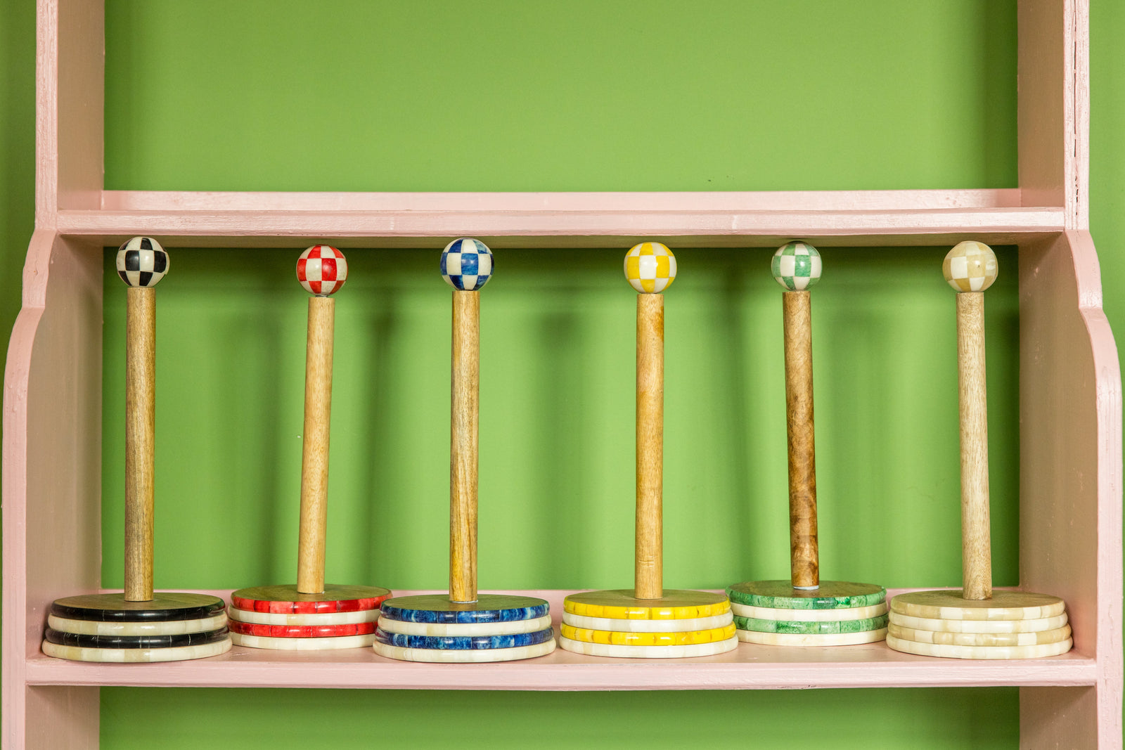 Set of wooden tumblers with colorful tops on a shelf against a green wall