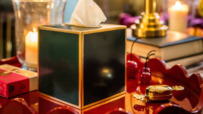 Decorative table setting with a tissue box, candles, and a lamp in a warm, blurred interior setting.