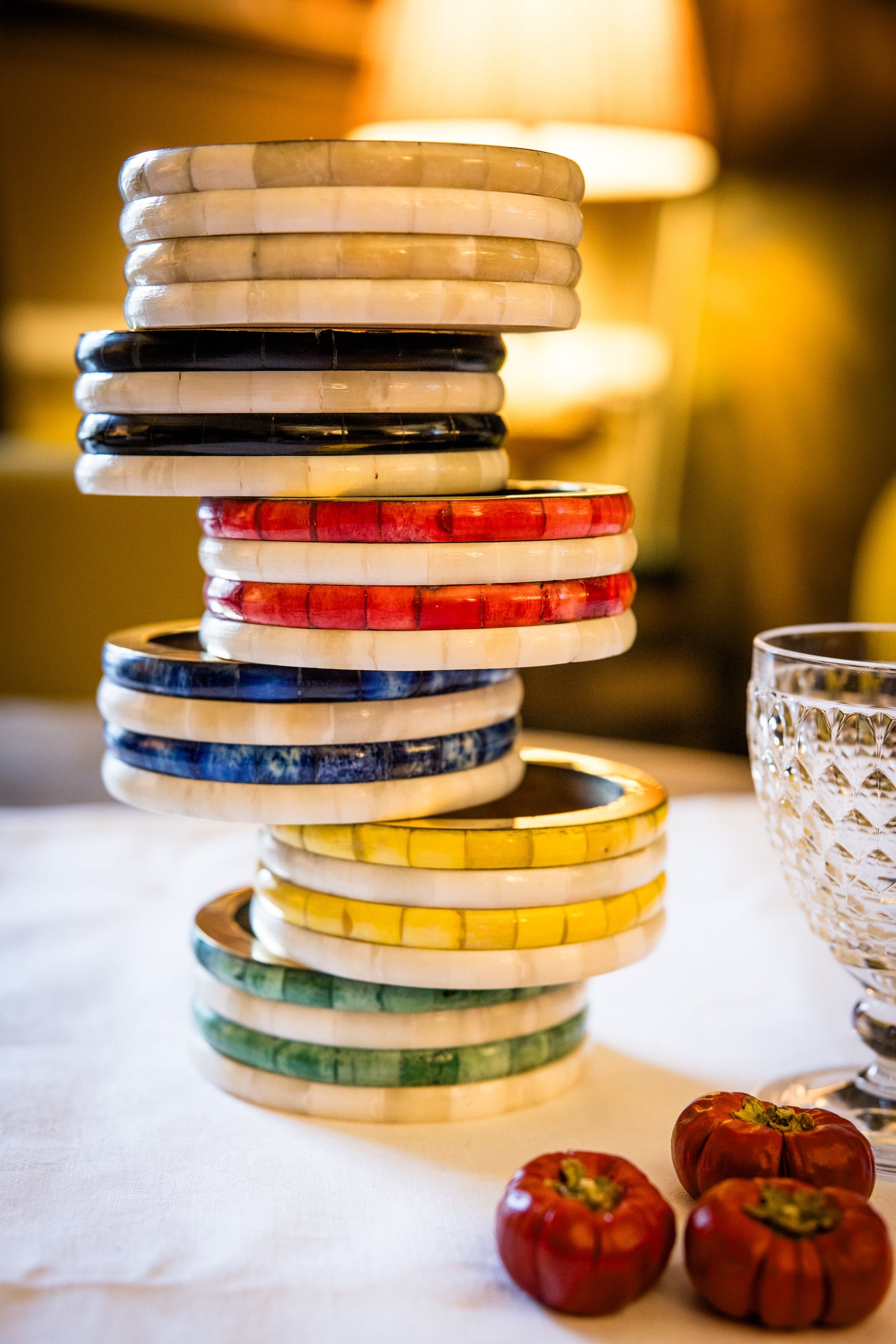 Stack of colorful ceramic plates on a table with decorative apples and a glass.