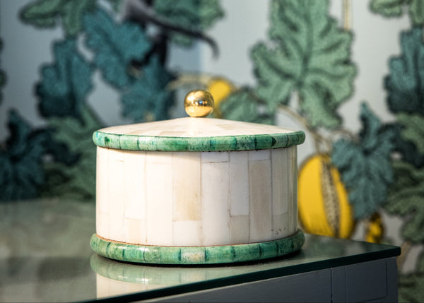 Decorative container with green lid on a surface against a leafy wallpaper background