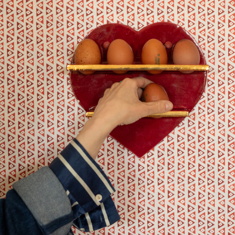 Red heart-shaped egg storage shelves with brown eggs being placed by a hand on a red patterned wall.