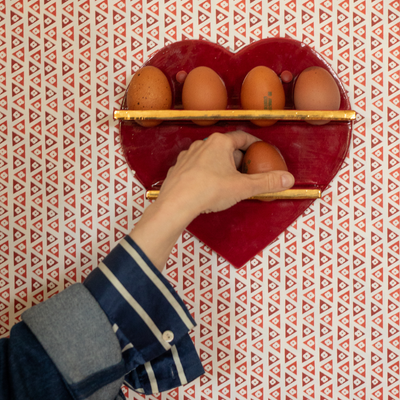 Red heart-shaped egg storage shelves with brown eggs being placed by a hand on a red patterned wall.