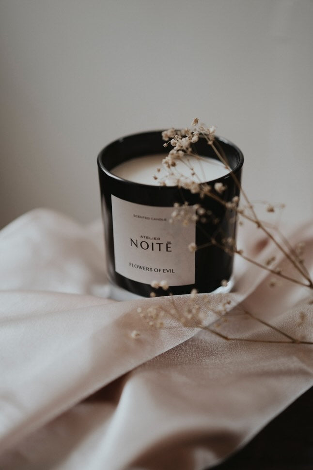 A candle in a black vessel on a light pink silk scarf
