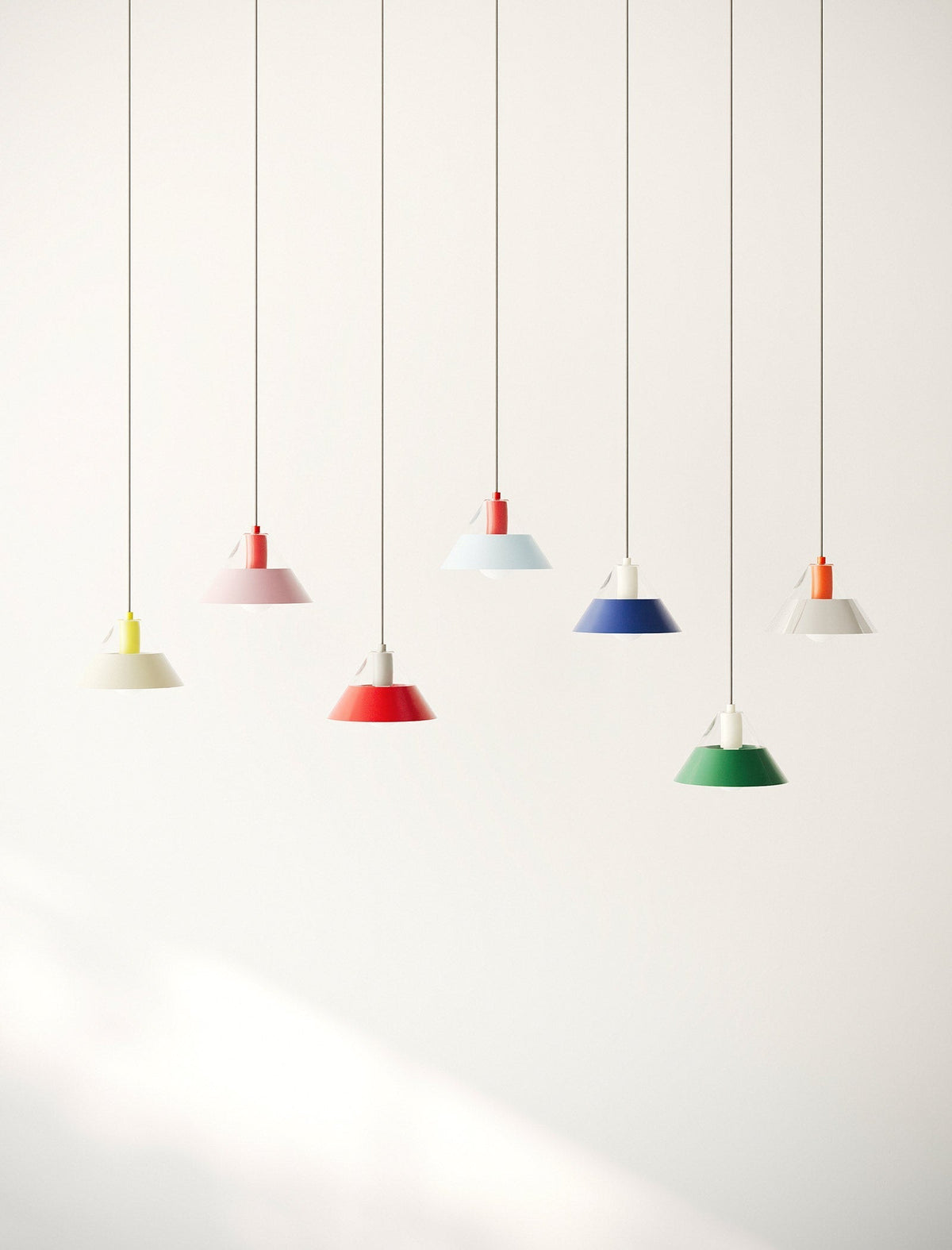 FIFTY FIFTY Lamp group of seven colorful pendant lamps with metal shades hanging against a white wall.