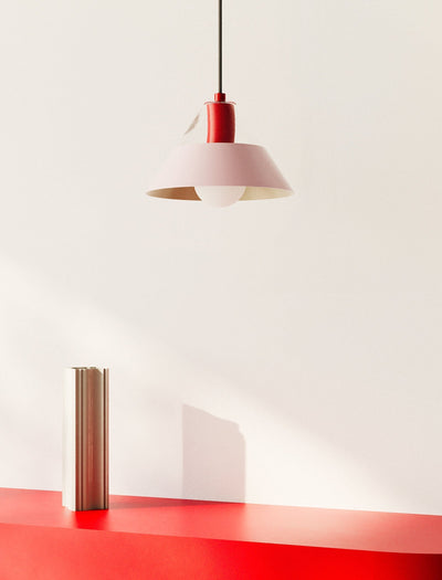 FIFTY FIFTY Lamp with a pink metal shade and red fixture hanging above a red surface and minimalist decor.