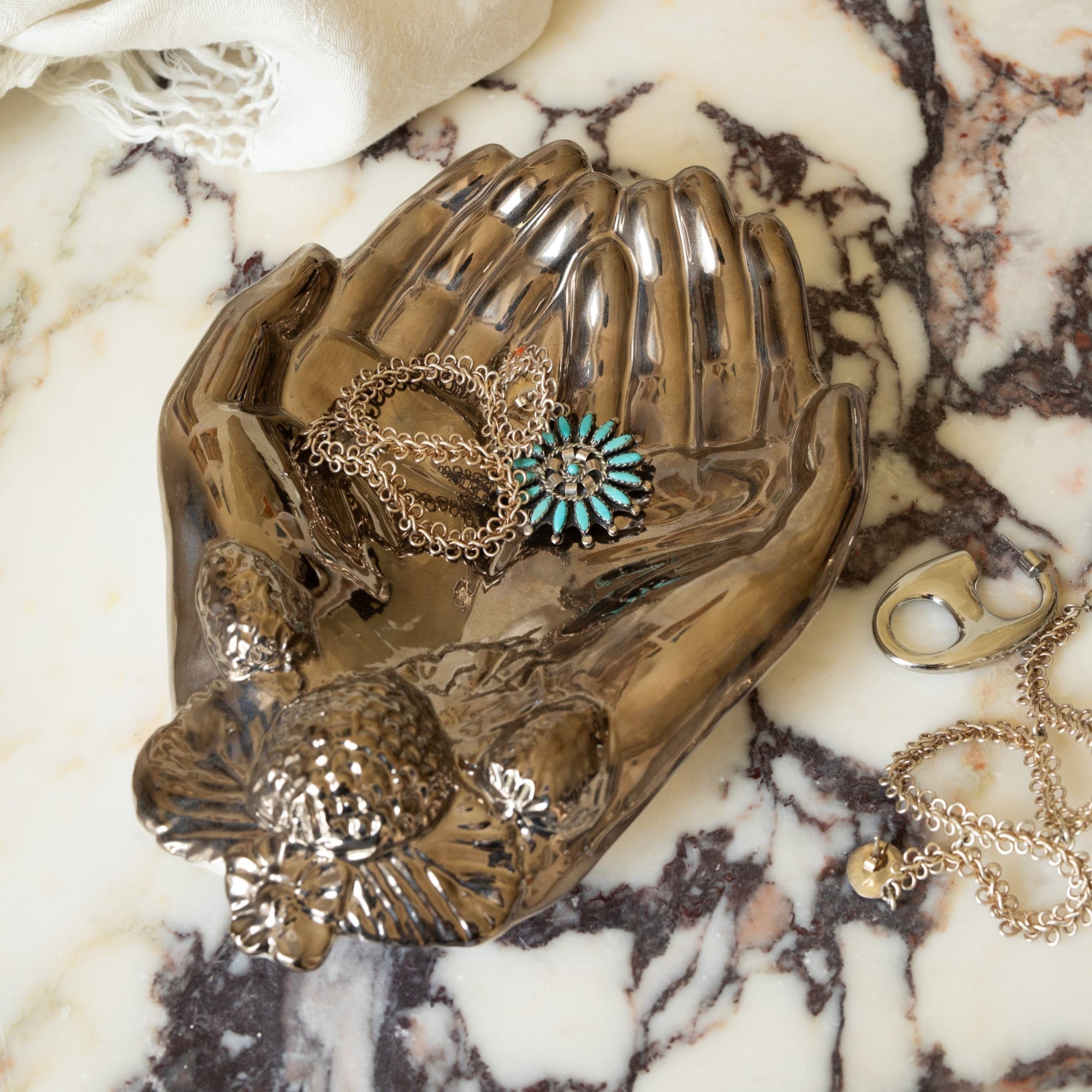 Decorative silver hand shaped dish with jewelry on a marble surface