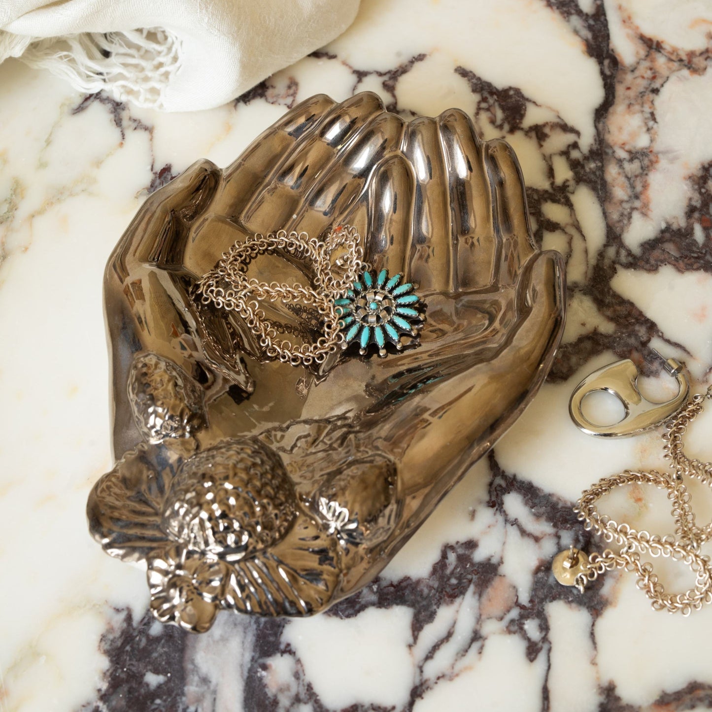 Decorative silver hand shaped dish with jewelry on a marble surface