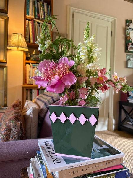 Hand-painted dark green diamond style planter with a pink edge holding fresh flowers on a bedside table in a colourful home.