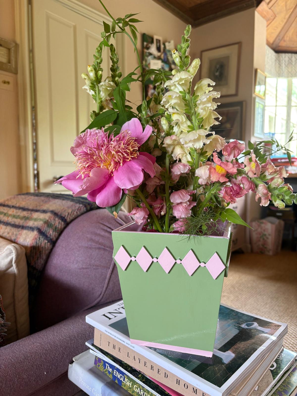 Hand-painted green diamond style planter with a light pink edge styled with fresh flowers on a bedside table in a colourful home.
