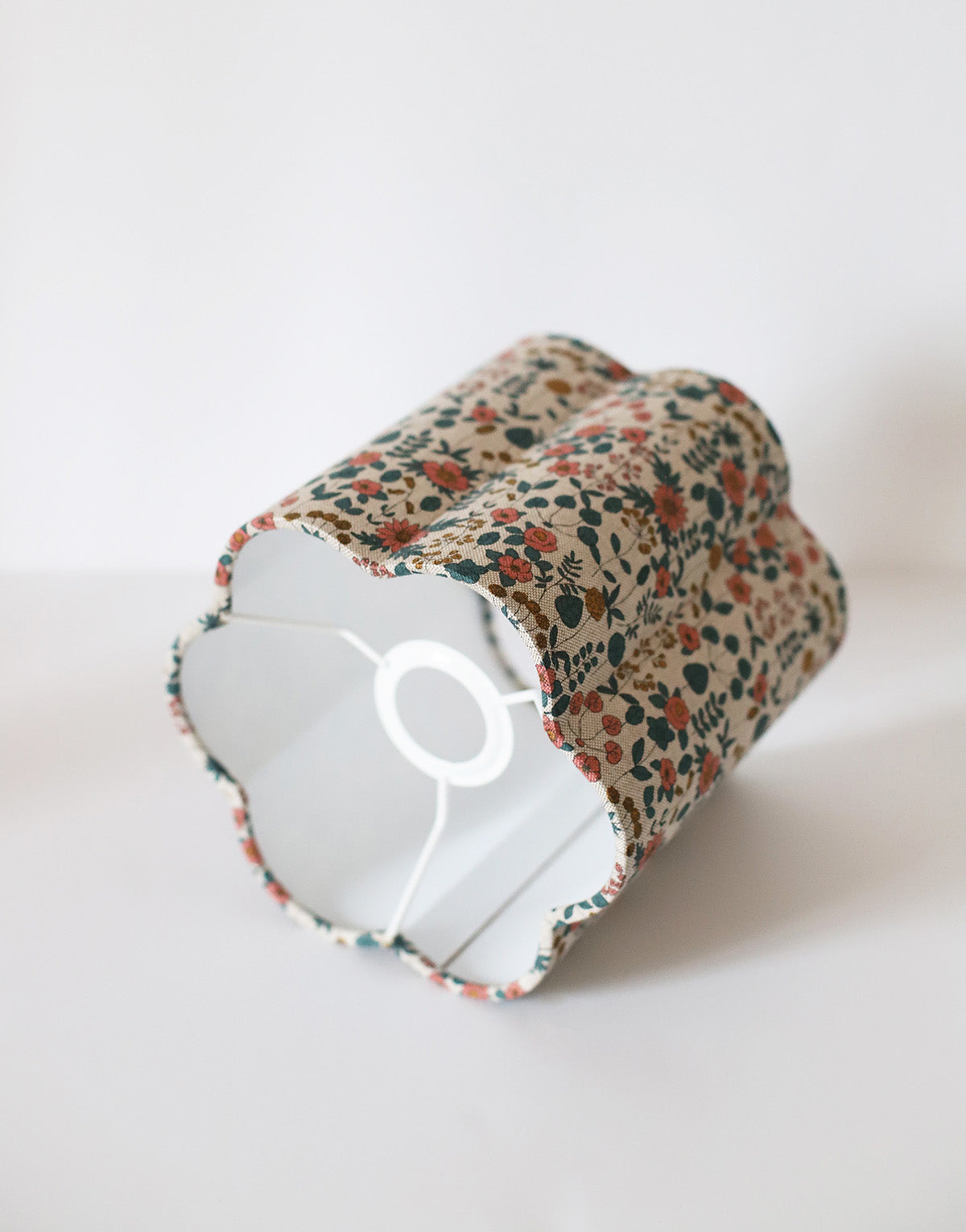 Abat-jour floral en coton beige, imprimé fleurs rouges et vertes, fait main, posé sur une surface blanche.