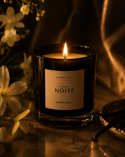 Candle in a black holder labeled 'Atelier Noète' with flowers and vanilla beans in the background.