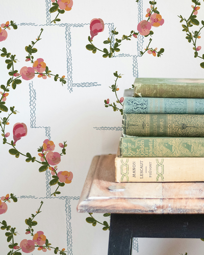 Stack of vintage books on a table with floral wallpaper in the background by Lizzet Frausto.