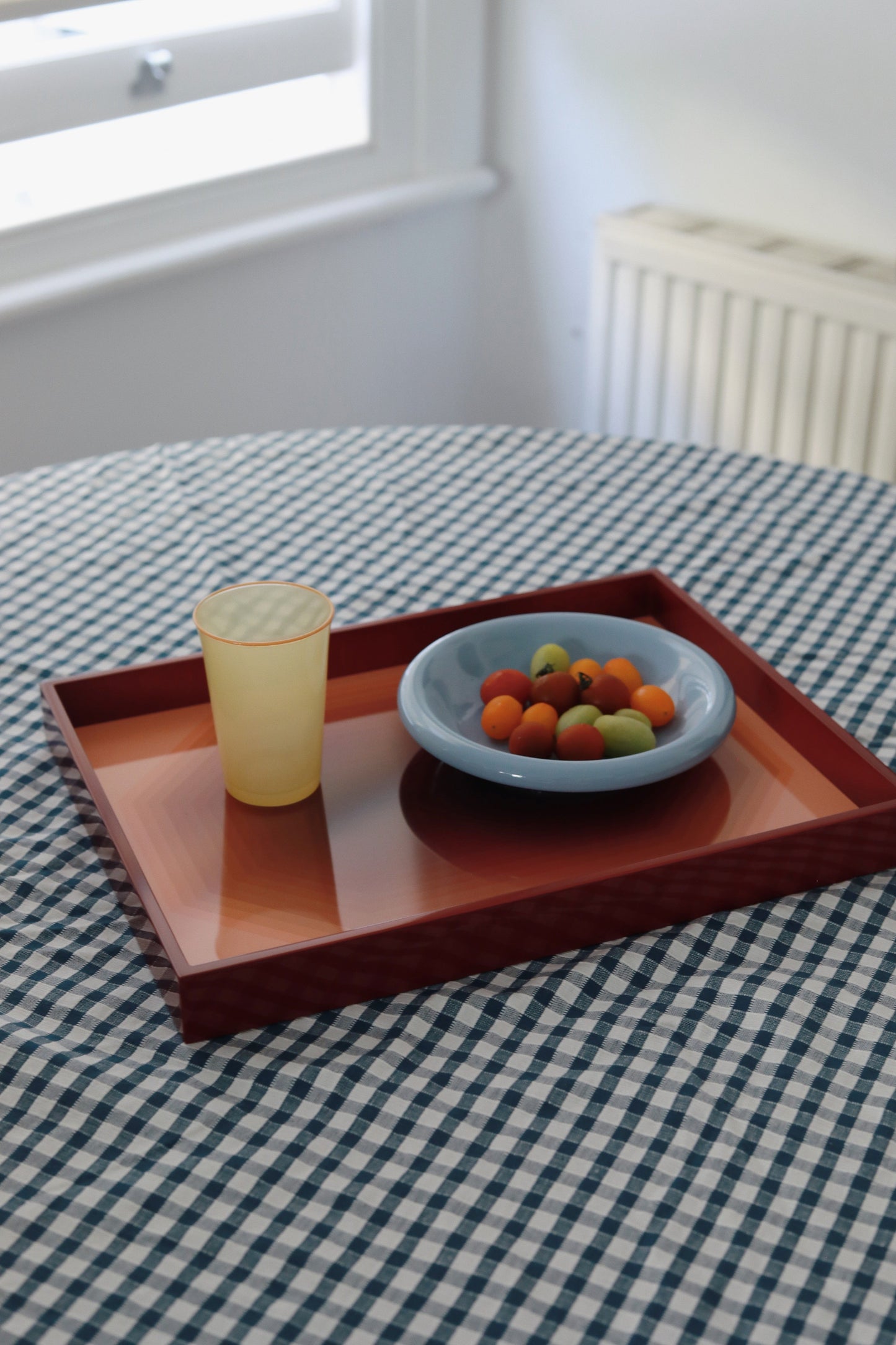 Vinidec Chiaroscuro high-gloss lacquer tray holding a glass and blue bowl of fruit on a blue gingham tablecloth