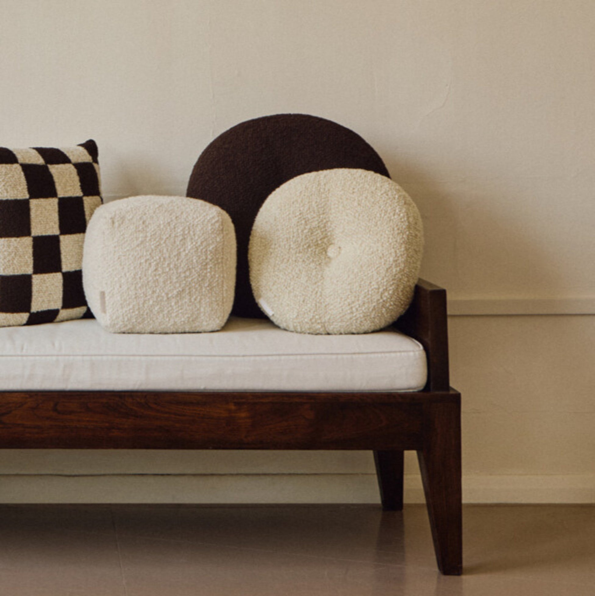 Lifestyle shot of brown wool bouclé round cushion with other cushions on daybed