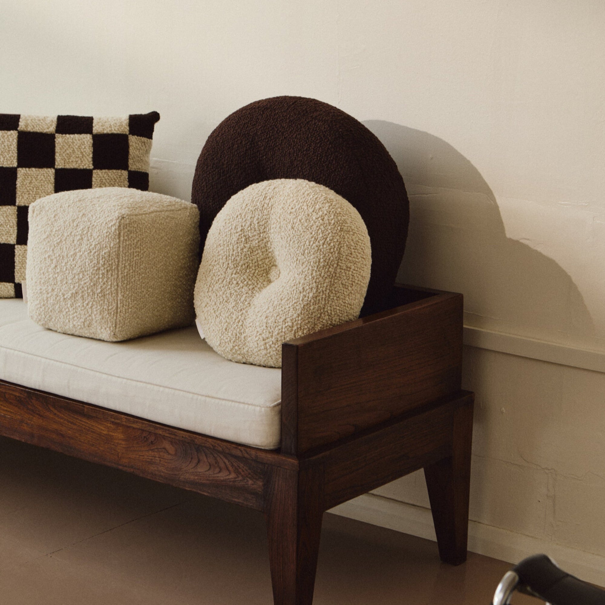 Lifestyle shot of cream wool bouclé cube cushion with round cushions on daybed