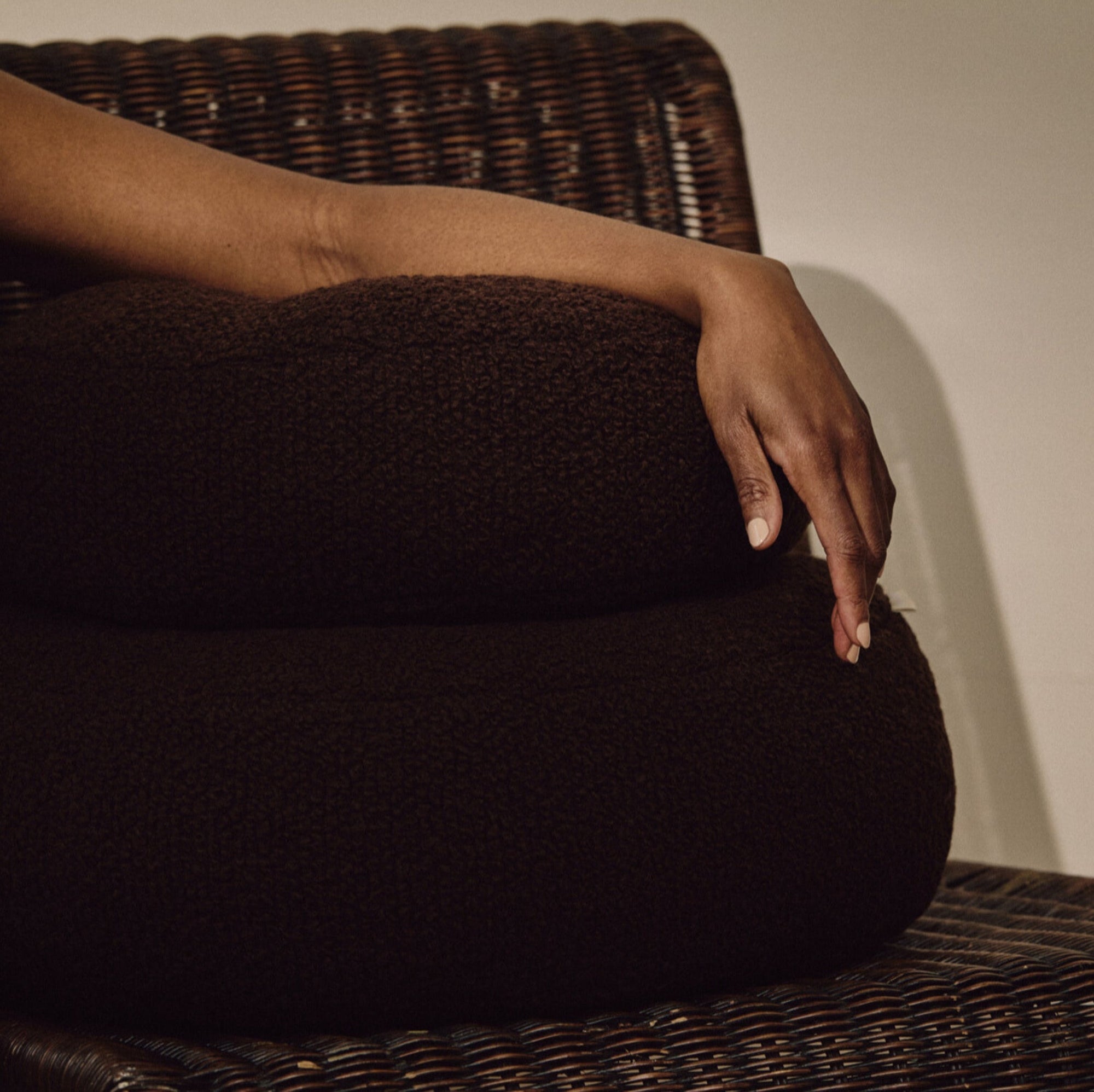 Lifestyle shot of arm resting on brown wool bouclé round cushion stack