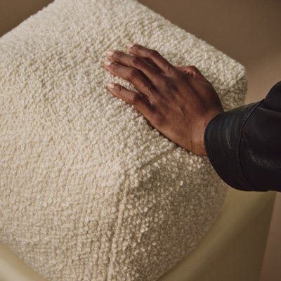 Lifestyle shot of hand resting on cream wool bouclé cube cushion