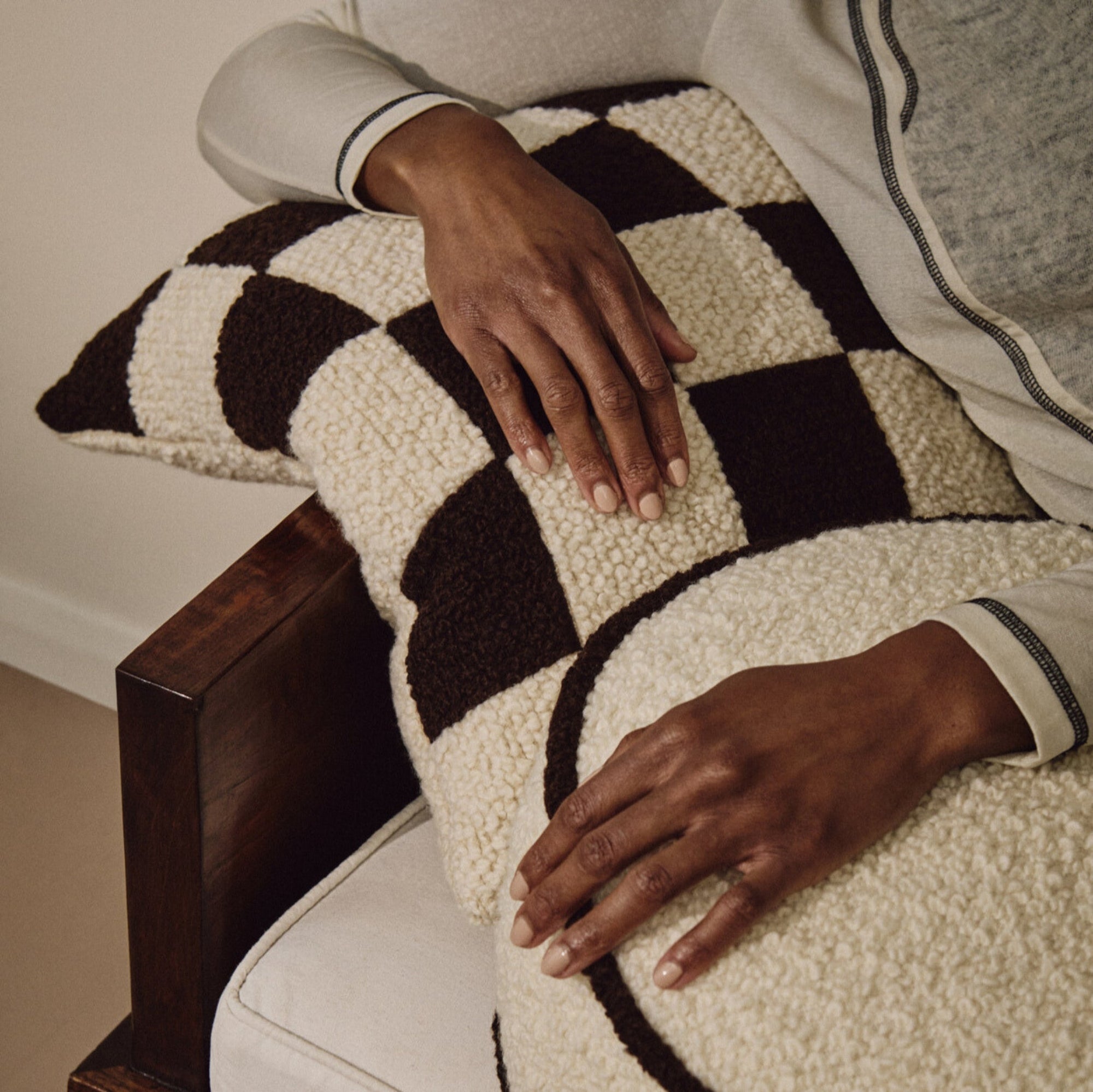 Lifestyle shot of hands resting on cream and brown wool bouclé checkered square cushion