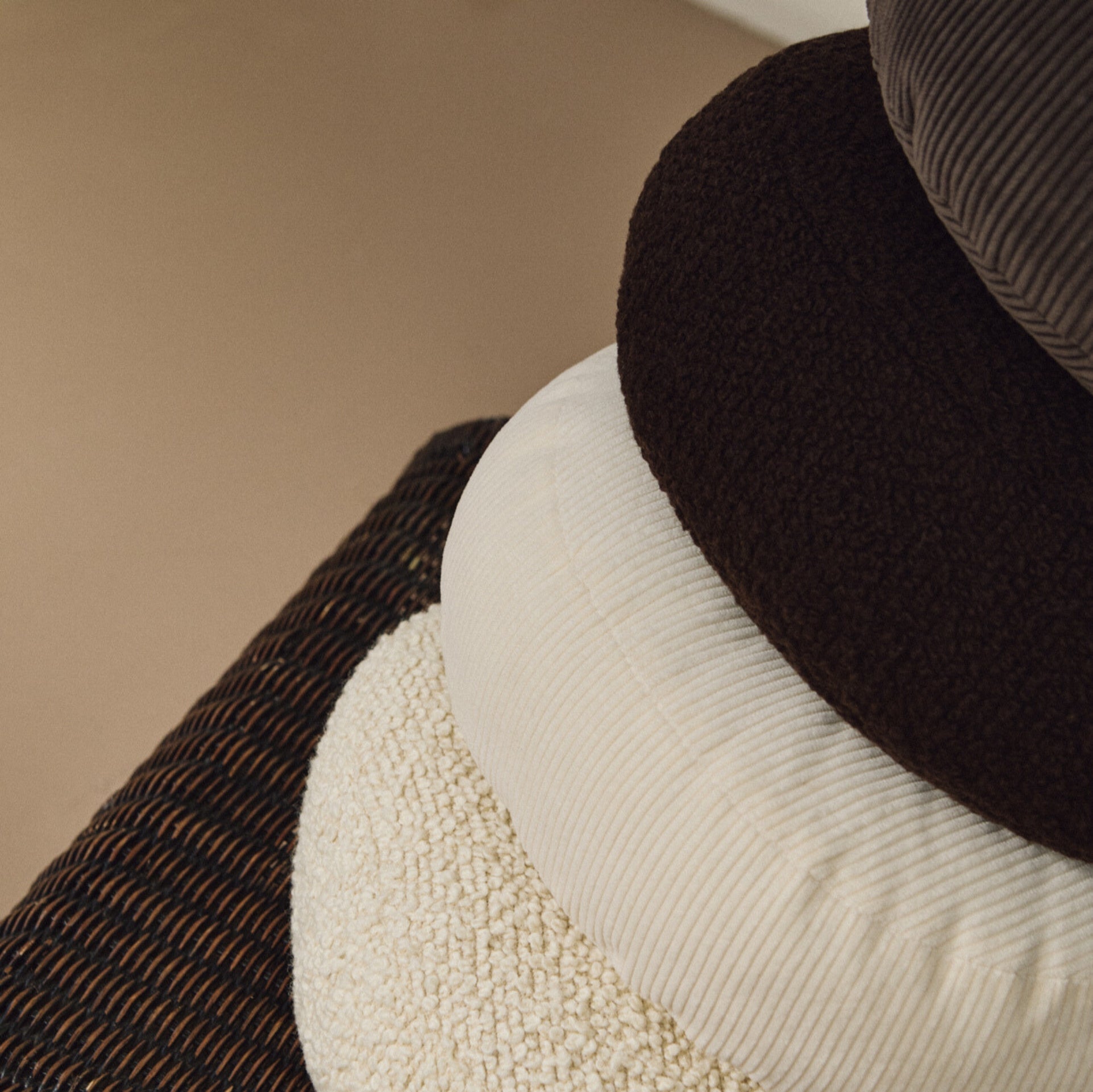 Lifestyle close up of stack of round wool and corduroy cushions on rattan chair