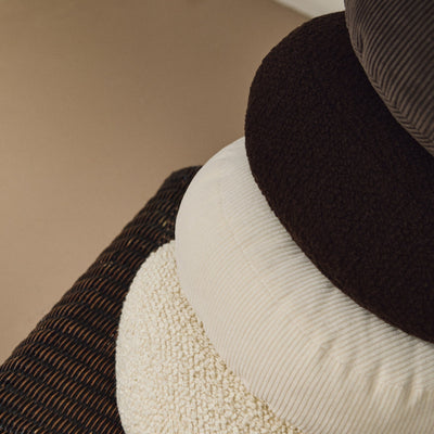 Lifestyle close up of stack of round wool and corduroy cushions on rattan chair