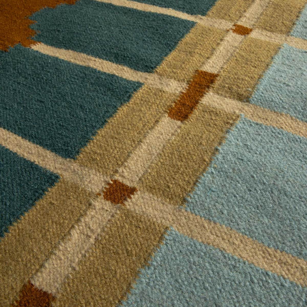 Close-up detail of Corbie handwoven flatweave wool rug showing geometric design in teal blue, light blue, ochre yellow and caramel brown tones.