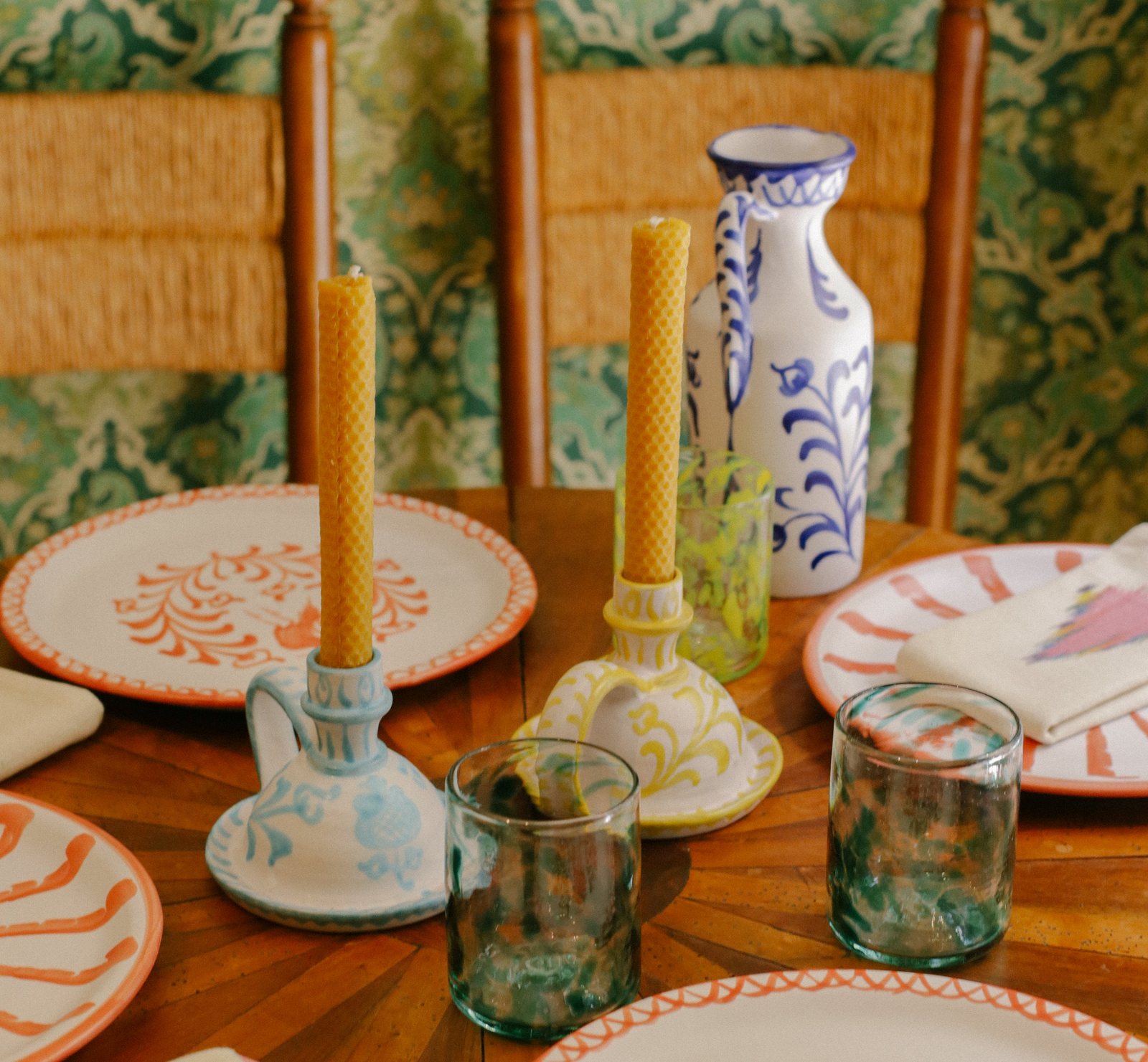 Dining table setting with ceramic plates, glasses, and a vase against a patterned wall. - lifestyle