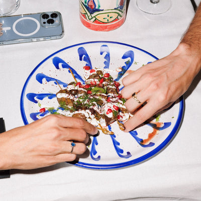 Two hands reaching towards a plate of food on a table with a phone and cup in the background. - lifestyle