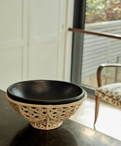 Amaranta black-clay bowl lifted from its handwoven Iraca palm nest