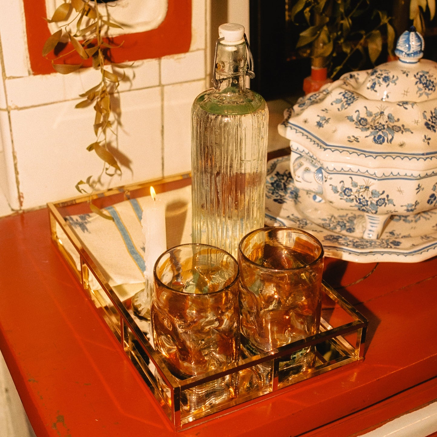 Two glasses with a bottle on a tray with a candle in the background - lifestyle