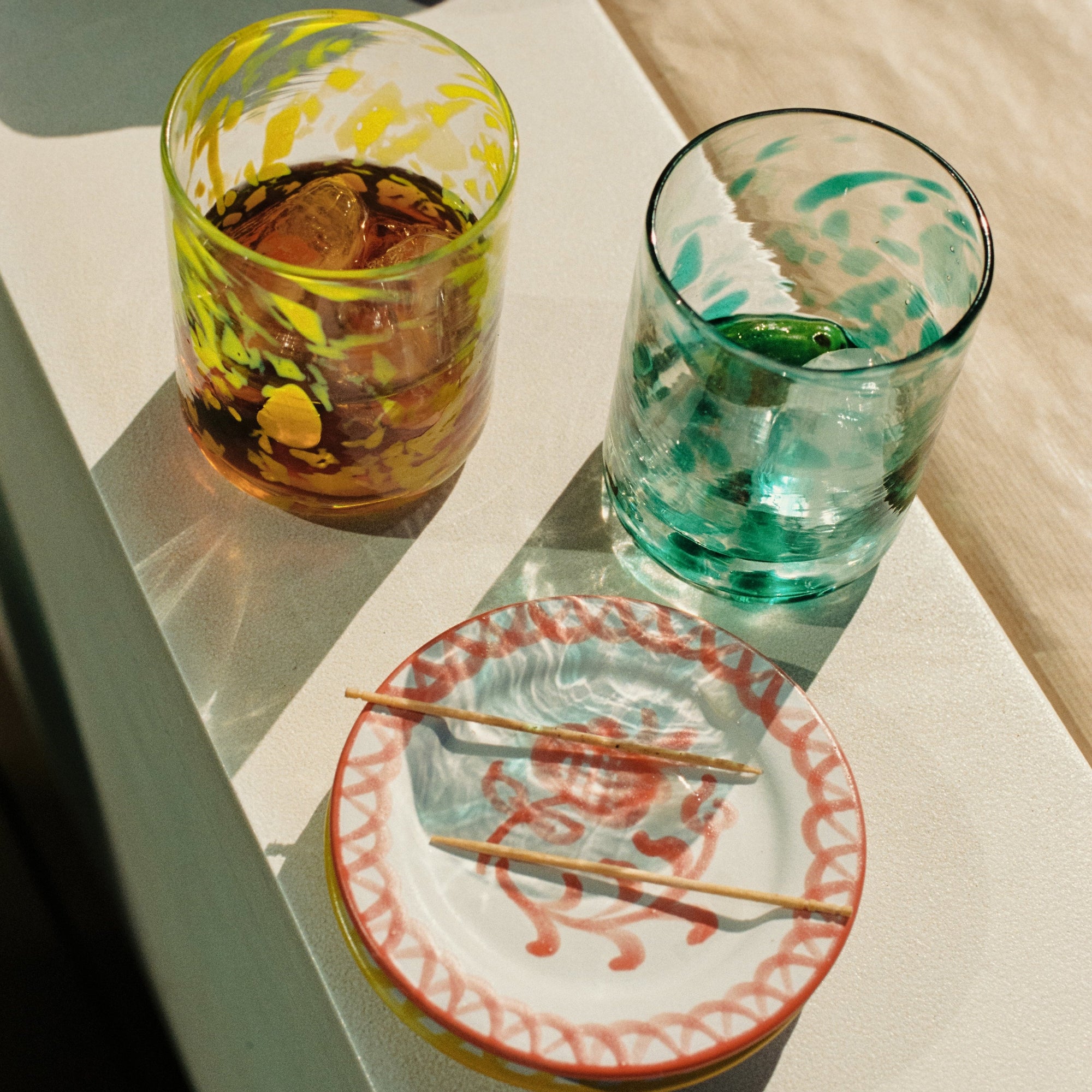 Two colorful spotted glasses with drinks on a light surface, accompanied by a small plate with chopsticks. - lifestyle