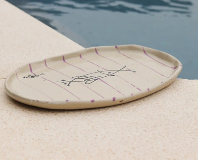 Ceramic plate with decorative fish design on a sandy surface near a pool.