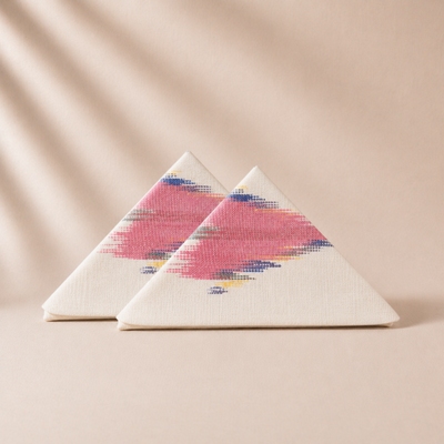 Two triangular napkin pieces with a colorful pink  pattern on a beige background