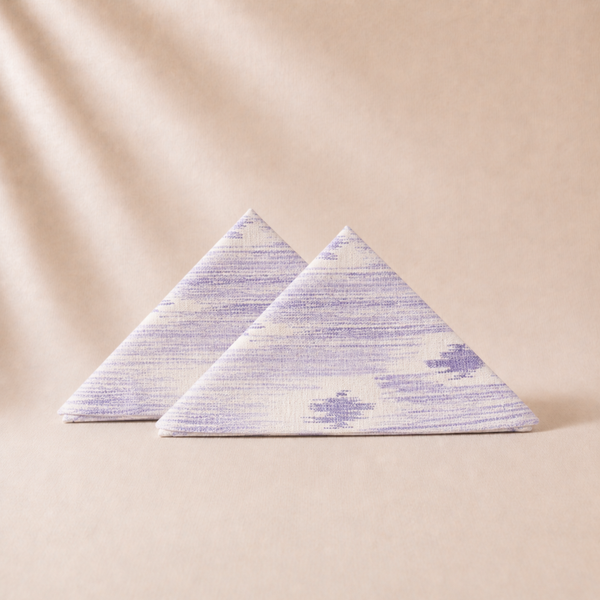 Two triangular fabric napkins with a subtle pattern on a beige background