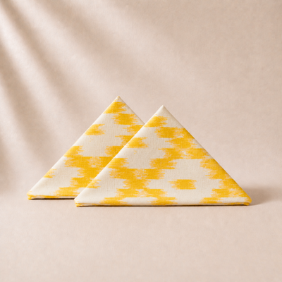 Two triangular napkins with yellow and white pattern on a beige background