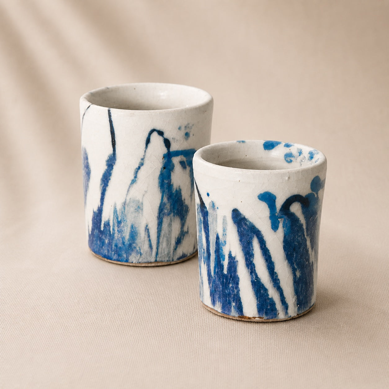 Two ceramic cups with blue and white abstract patterns on a beige background