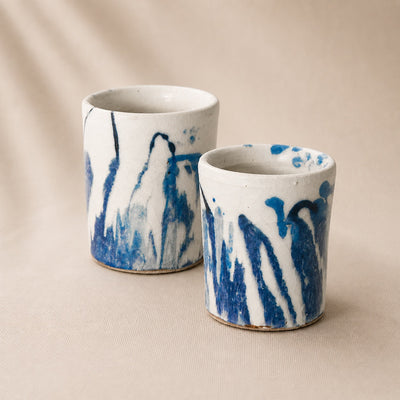 Two ceramic cups with blue and white abstract patterns on a beige background