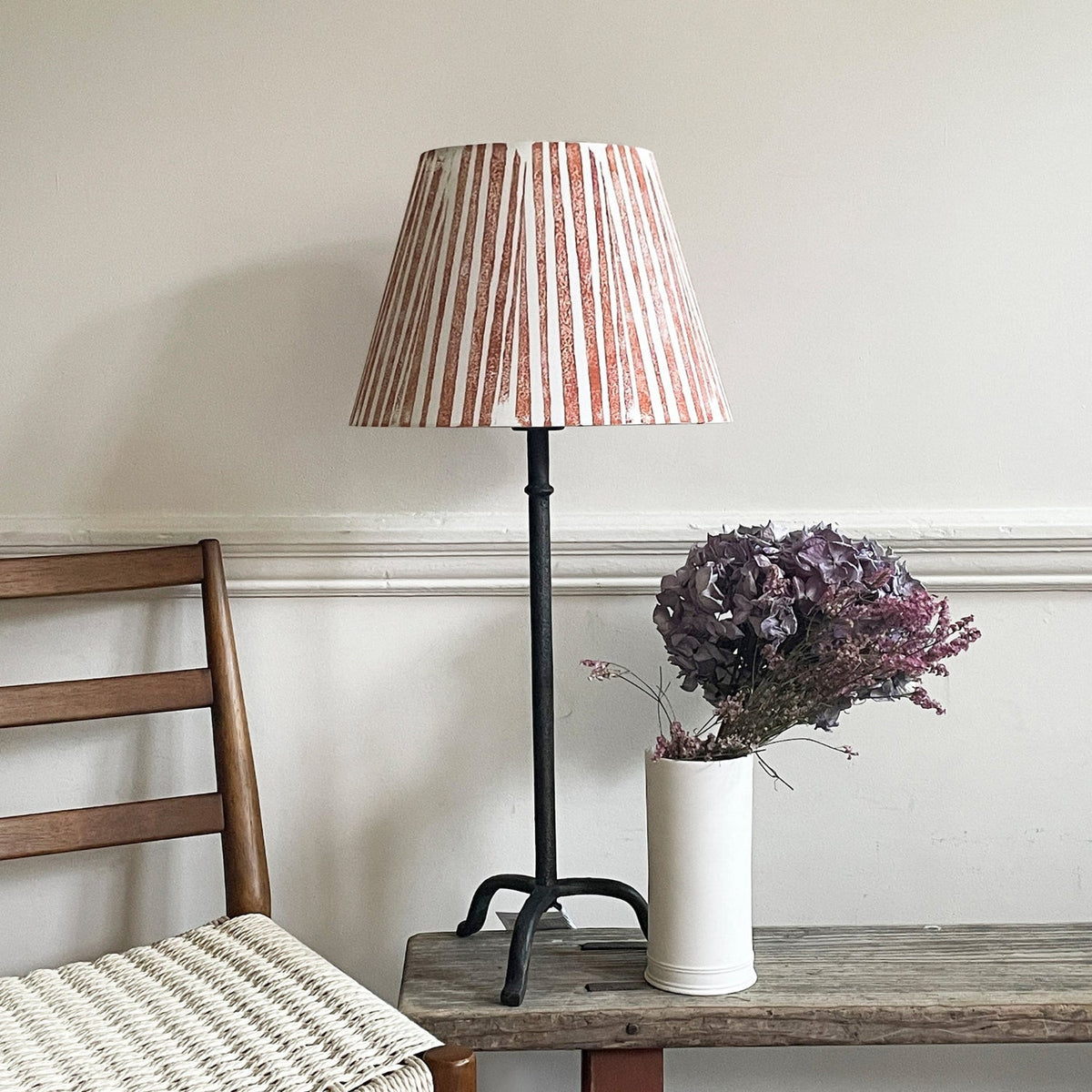 Empire light shade in a bold stripe design with orange and cream tones, styled on a tall metal lamp beside a modern chair. A colourful lampshade for modern interiors, perfect for striped lampshades UK collections.