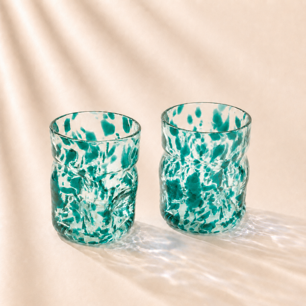 Two green and white marbled glass tumblers on a beige background