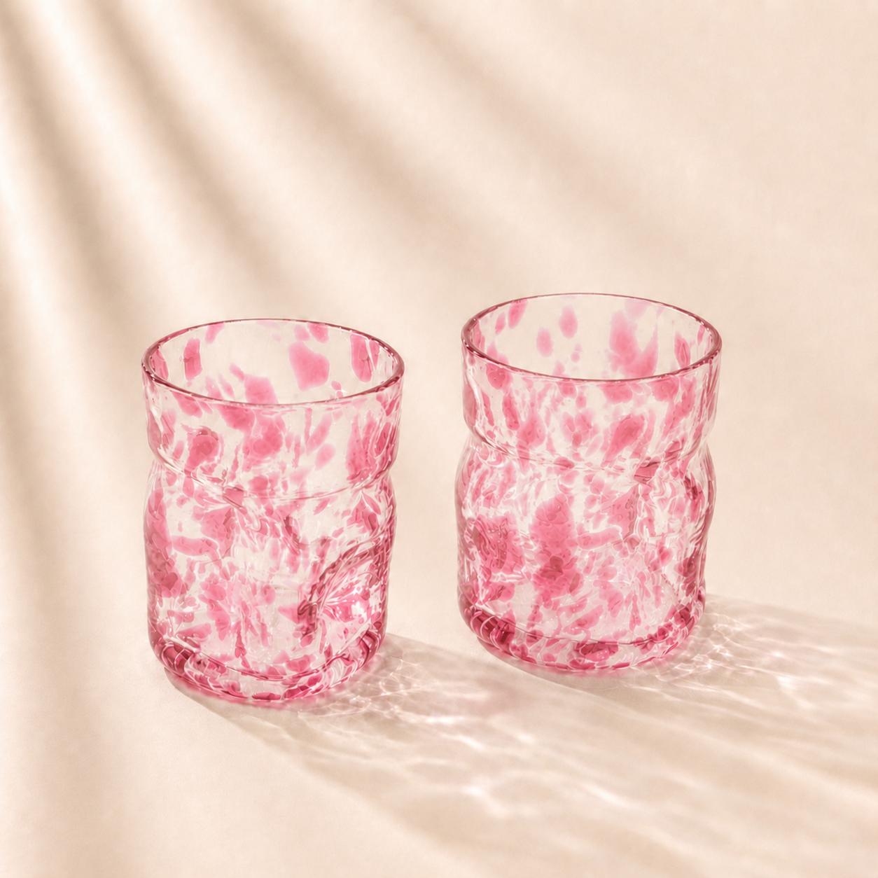 Two pink marbled glass tumblers on a beige background