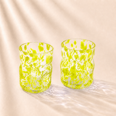 Two green glass tumblers on a beige fabric background